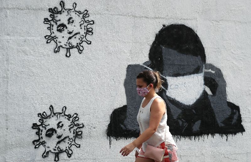 A woman walks past by a graffiti depicting Brazil's President Jair Bolsonaro adjusting his protective face mask and viruses, amid the coronavirus disease (COVID-19) outbreak in Rio de Janeiro, Brazil July 2, 2020. REUTERS/Sergio Moraes